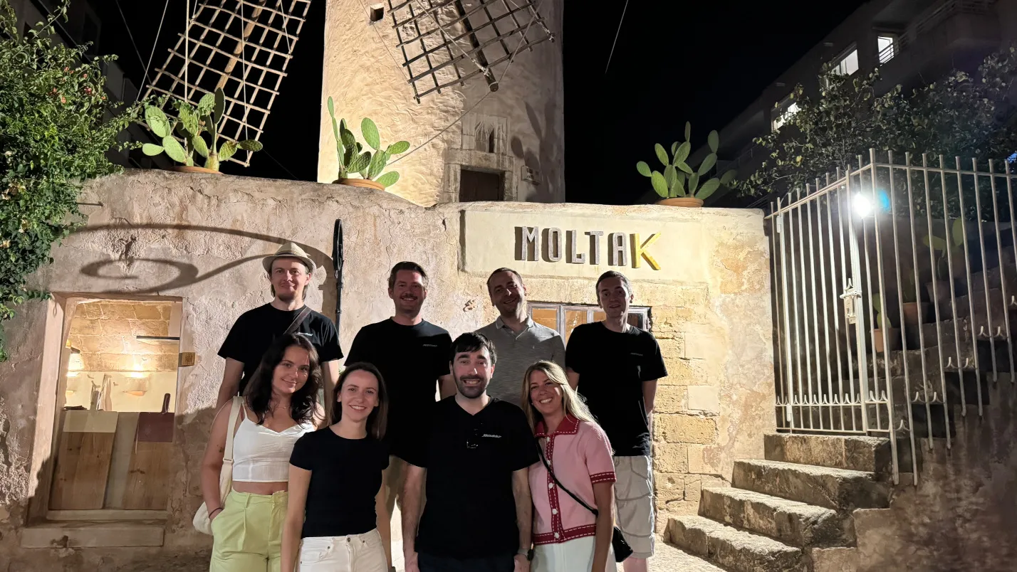 Das appsoluts-Team steht abends vor einem historischen Gebäude mit Windmühle, lacht in die Kamera. Gemeinsamer Moment während der Workation.